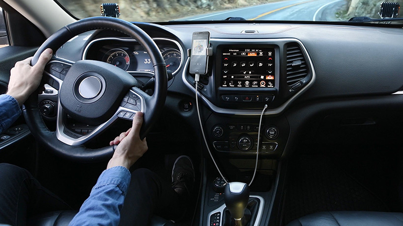 Person driving a car, holding the steering wheel, with a phone on the dashboard.