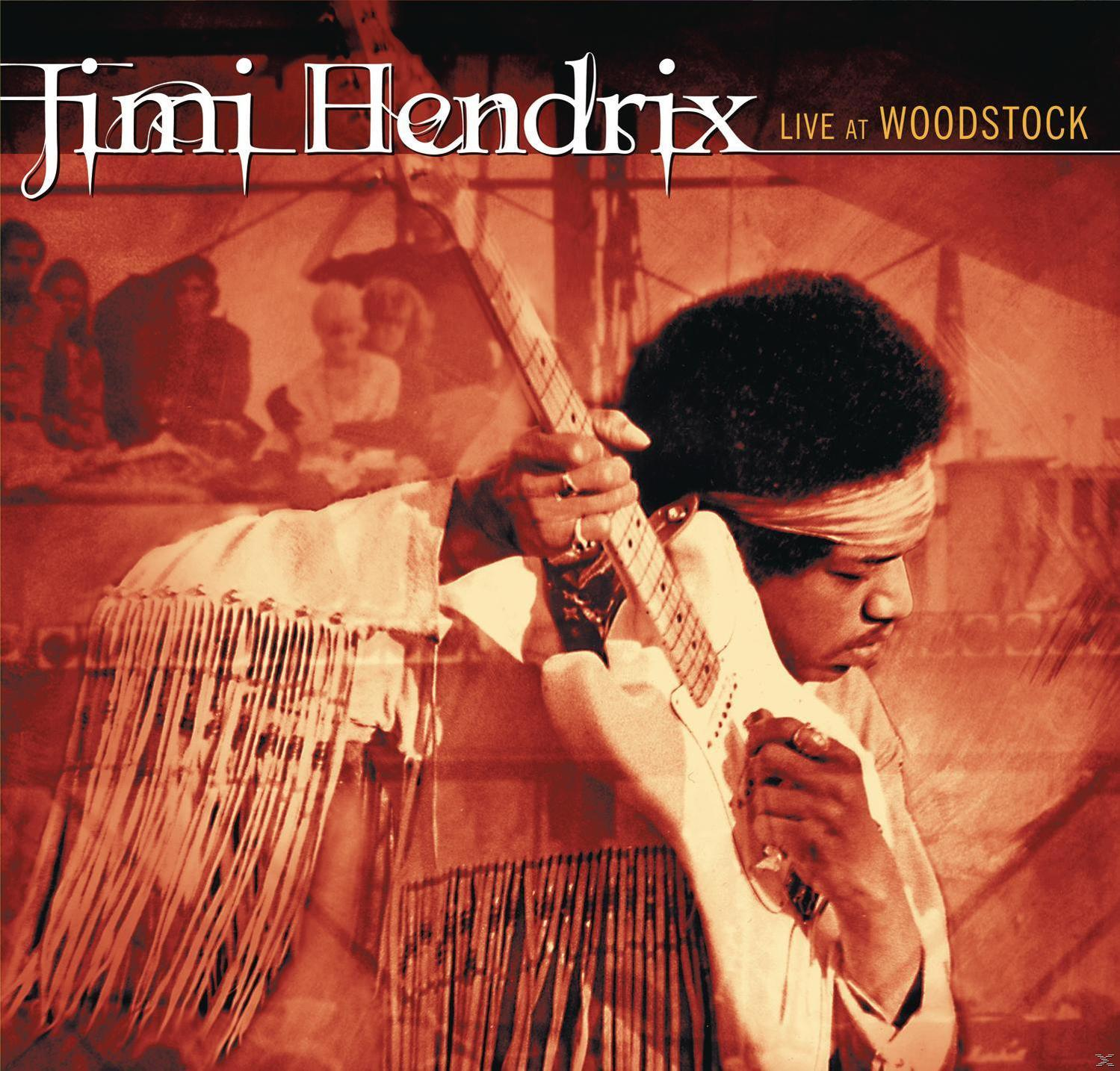 Jimi Hendrix élőben a Woodstock-on, fehér gitáron játszik, vörös árnyalatú háttérrel.