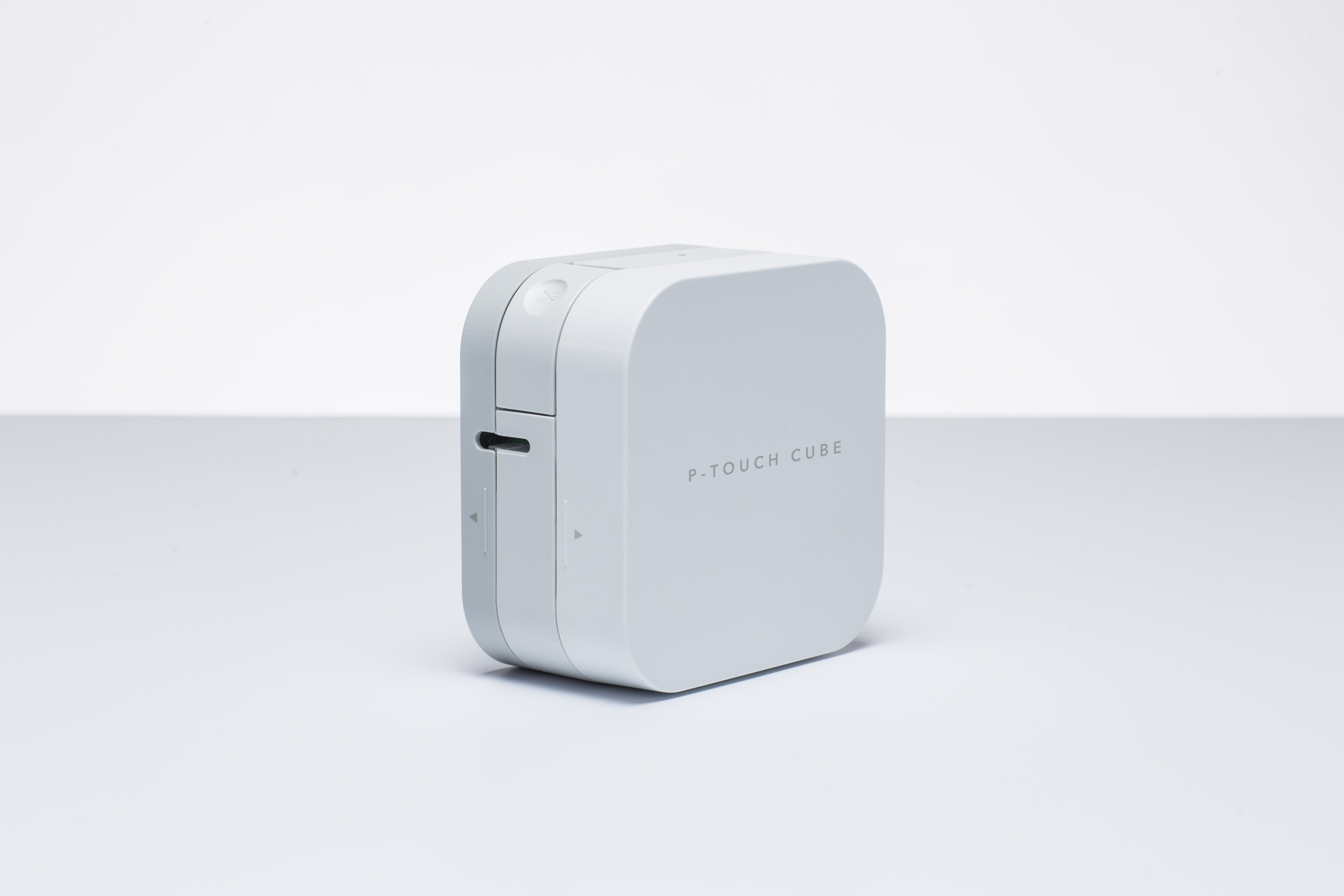 Weißer P-Touch Cube Etikettendrucker. Quadratisches, weißes Gerät mit Schlitz für Etiketten, schlichtes Design.