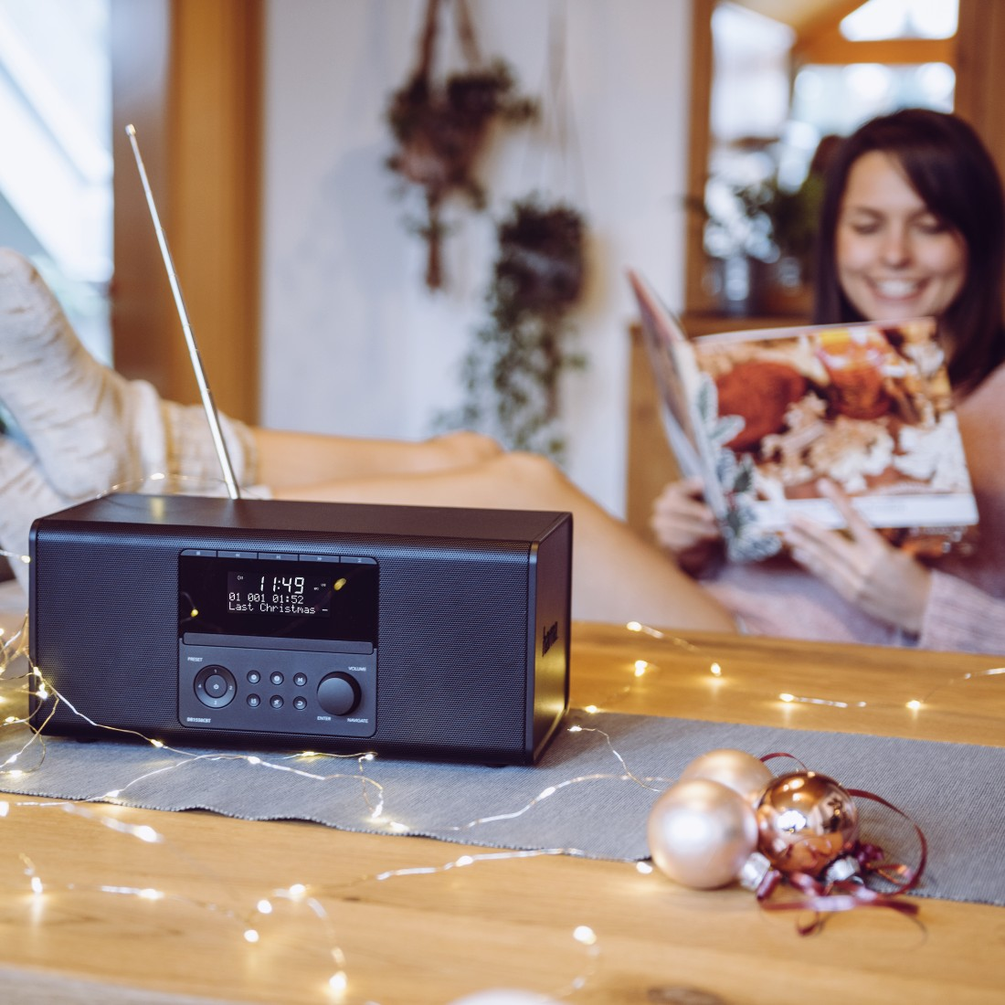 Femme lisant magazine près radio, décorations Noël sur table.
