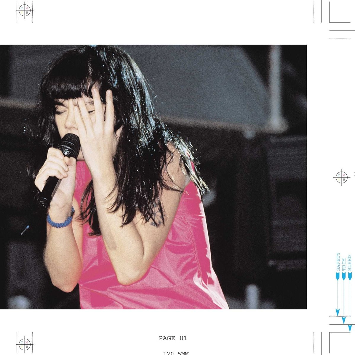 Une femme aux cheveux noirs chante dans un micro, portant un haut rose et un bracelet bleu.