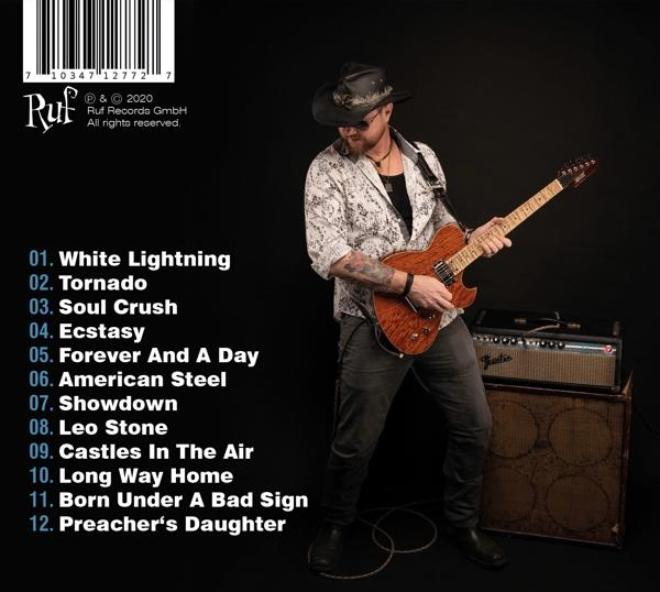 Ein Mann spielt Gitarre auf einer Bühne mit einer Liste von Titeln. Die Bühne hat einen Lautsprecher.