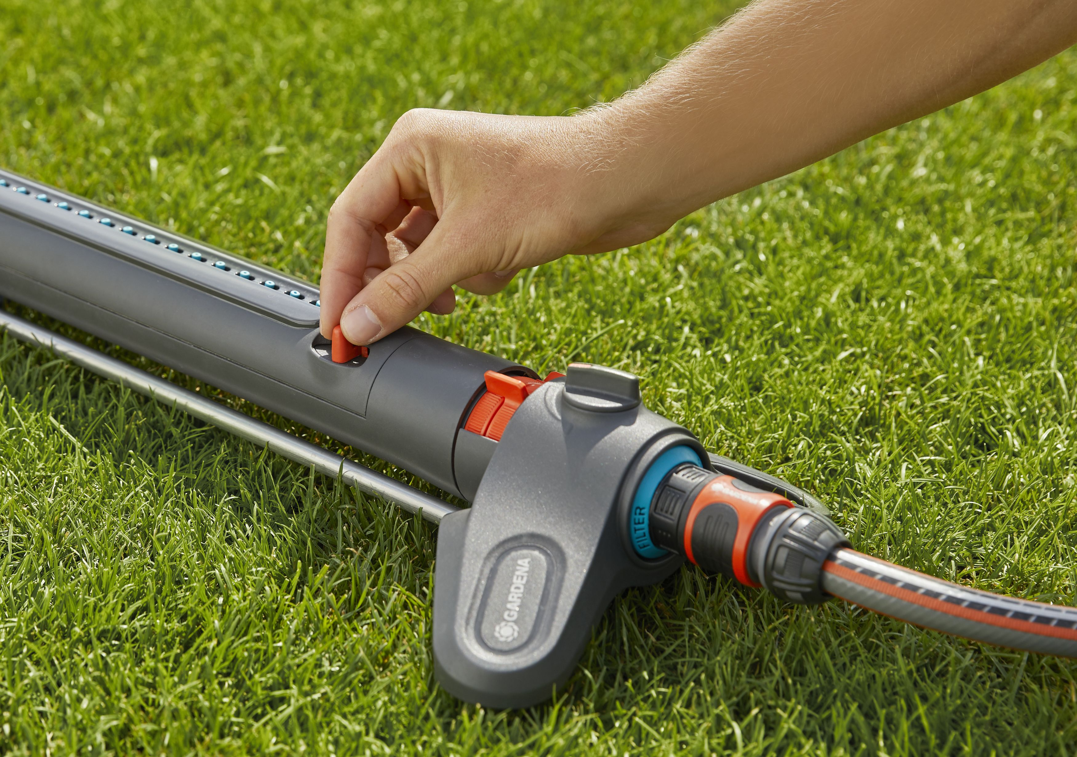 Eine Hand, die einen Gartensprenger auf grünem Gras einstellt.