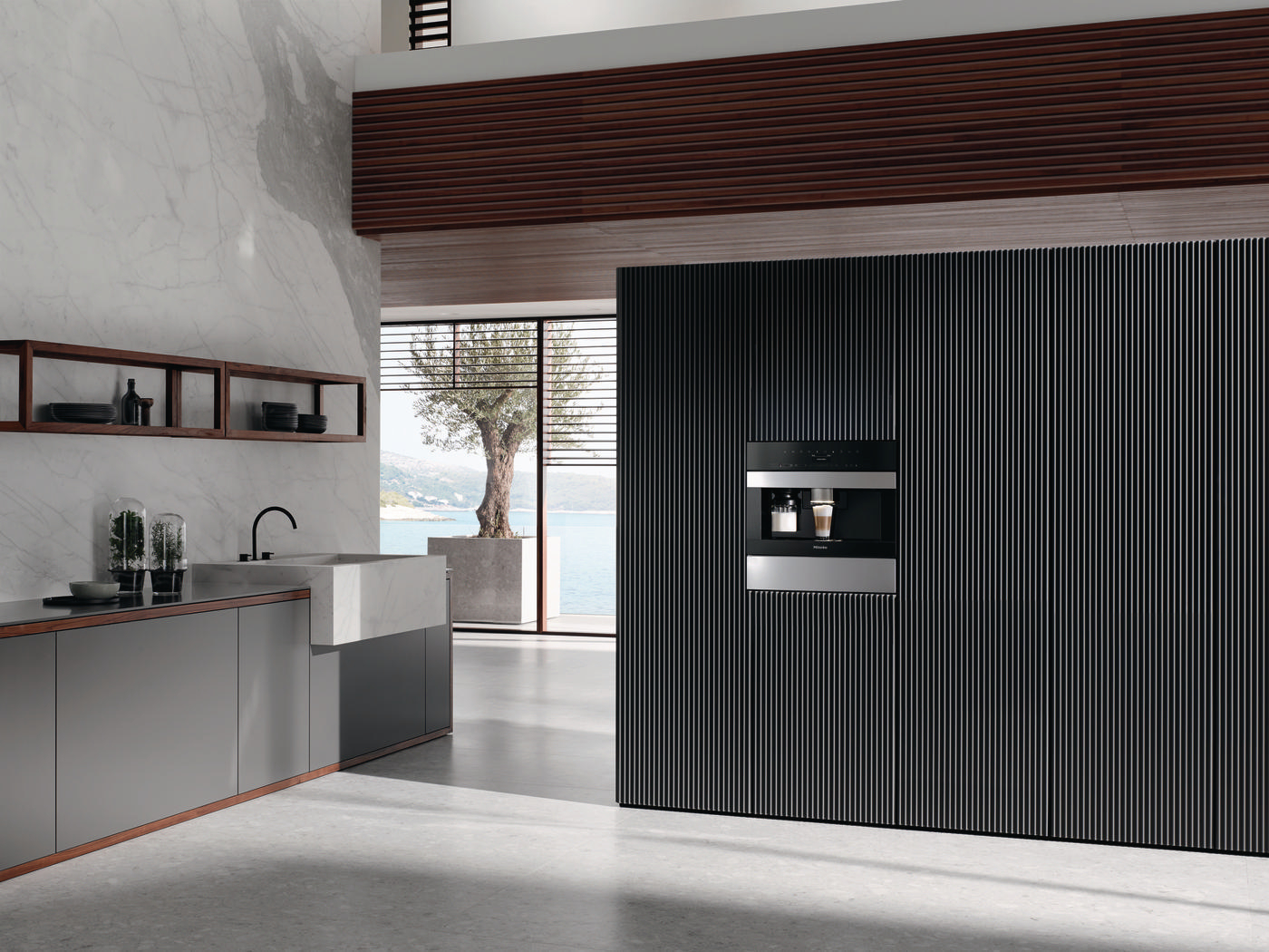 Eine moderne Küche mit einer Kaffeemaschine in einer schwarzen Wand. Die Landschaft ist durch ein Fenster zu sehen.