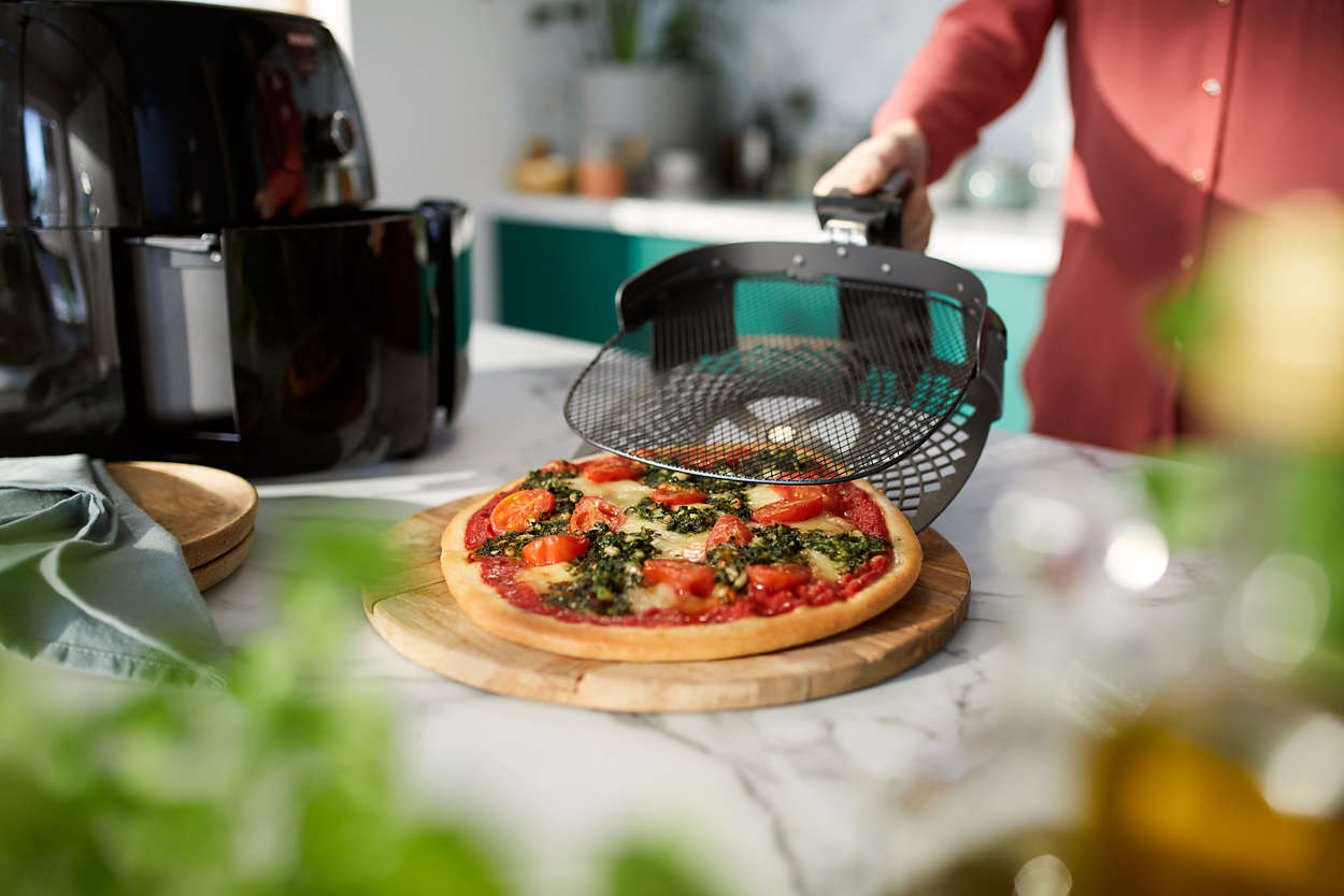 Une pizza est retirée d'une friteuse à air. Une personne tient le panier avec la pizza.