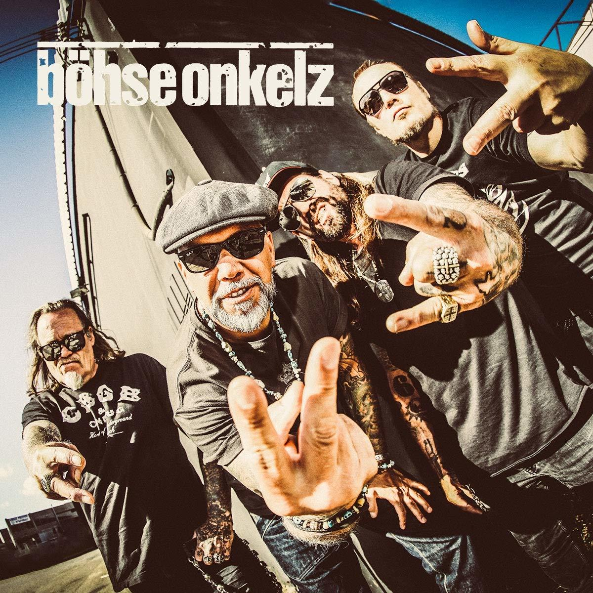 Vier Männer mit Sonnenbrillen, die posieren. Einer zeigt einen Mittelfinger. Der Bandname steht oben.