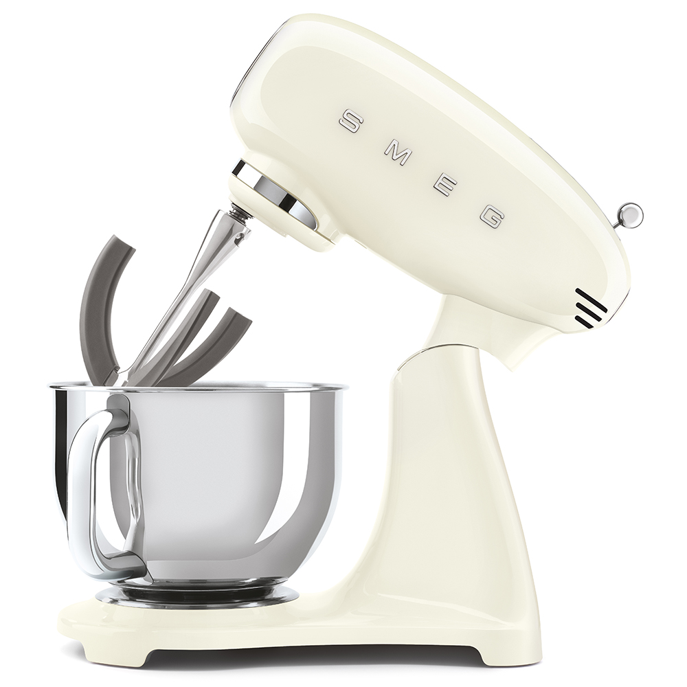 Ein cremefarbener Smeg-Küchenmixer mit einer silbernen Schüssel und Aufsätzen, auf weißem Grund.