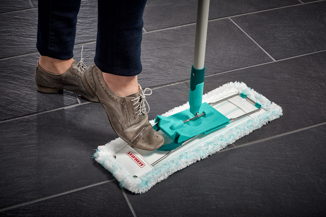 Une personne marchant sur une serpillère Leifheit sur un sol carrelé noir.