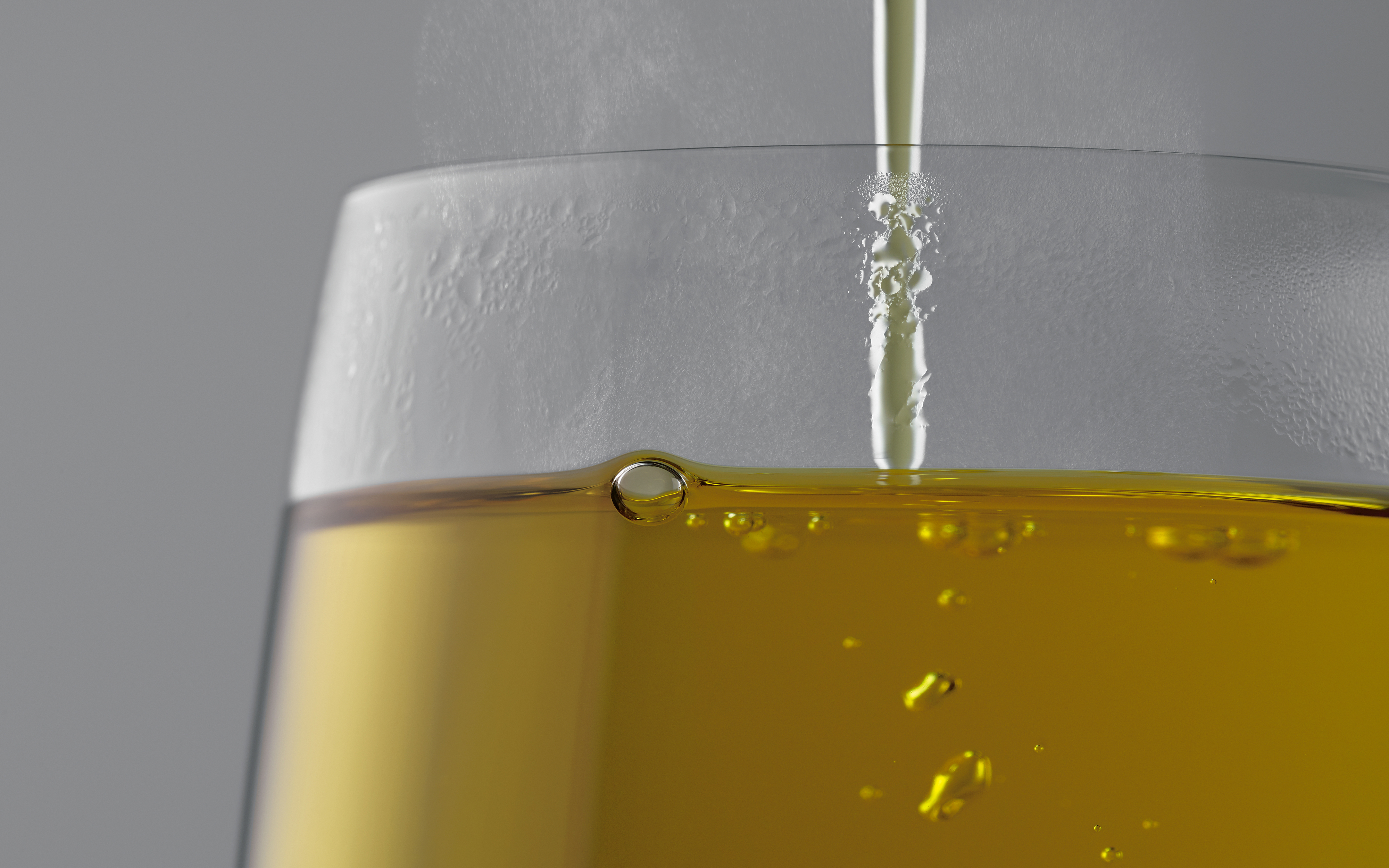 Ein Glas mit Flüssigkeit, ölartig, mit Blasen. Das Glas ist klar, der Hintergrund grau.
