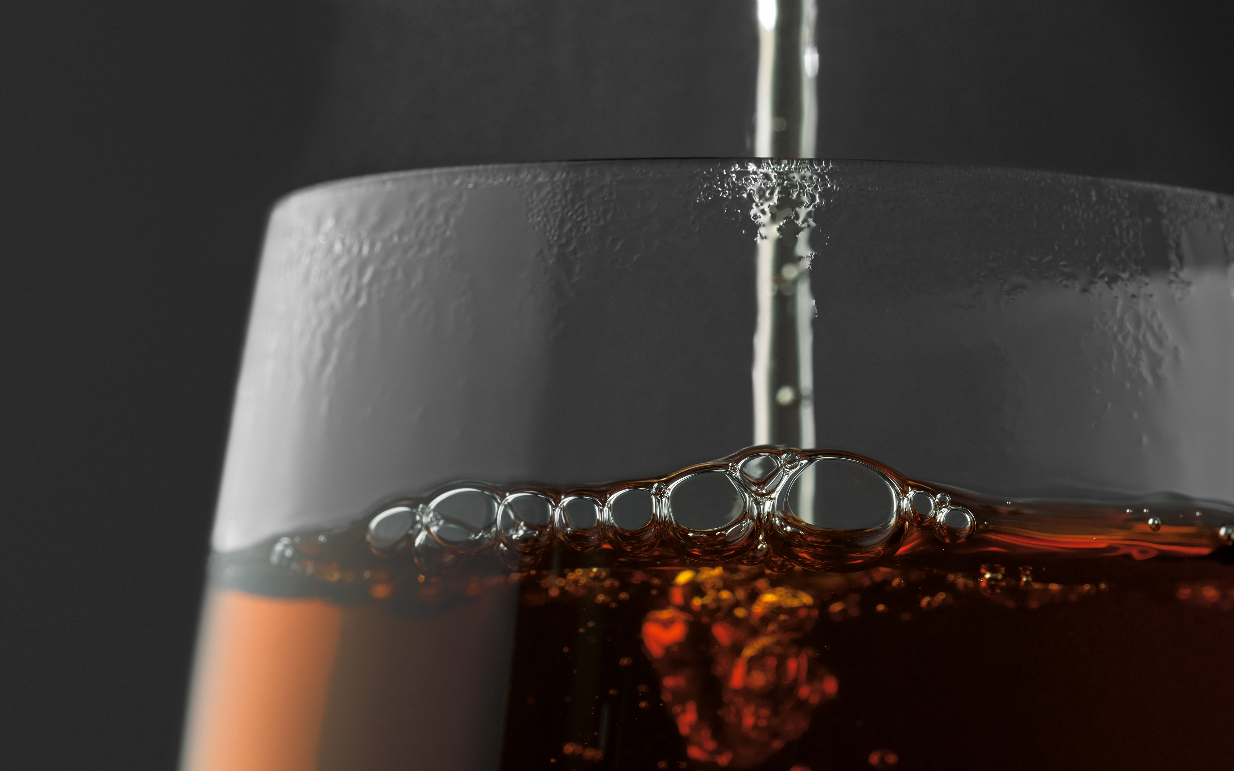 Ein Glas wird mit einer dunklen Flüssigkeit gefüllt. Blasen sind oben sichtbar.