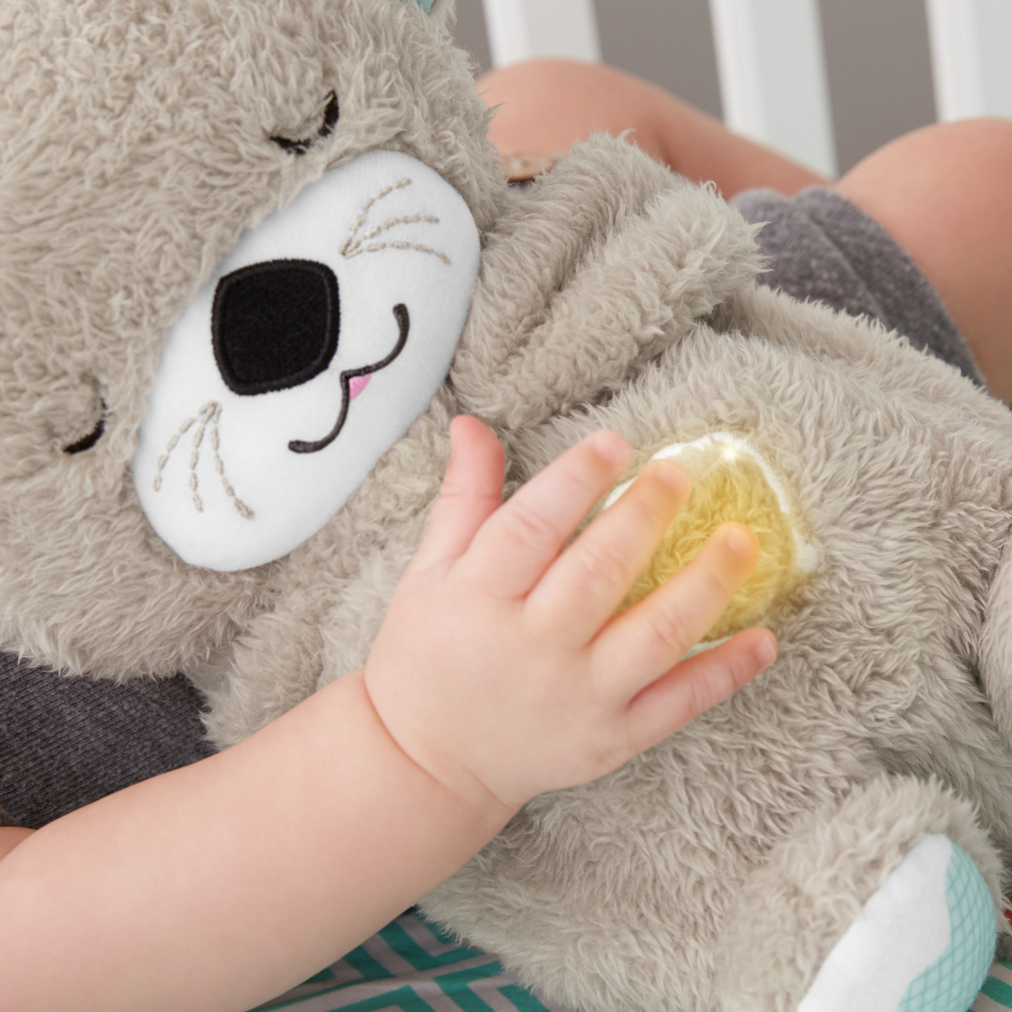 Babyhand auf einem grauen Stoffotter, mit gelbem Licht auf dem Spielzeug.