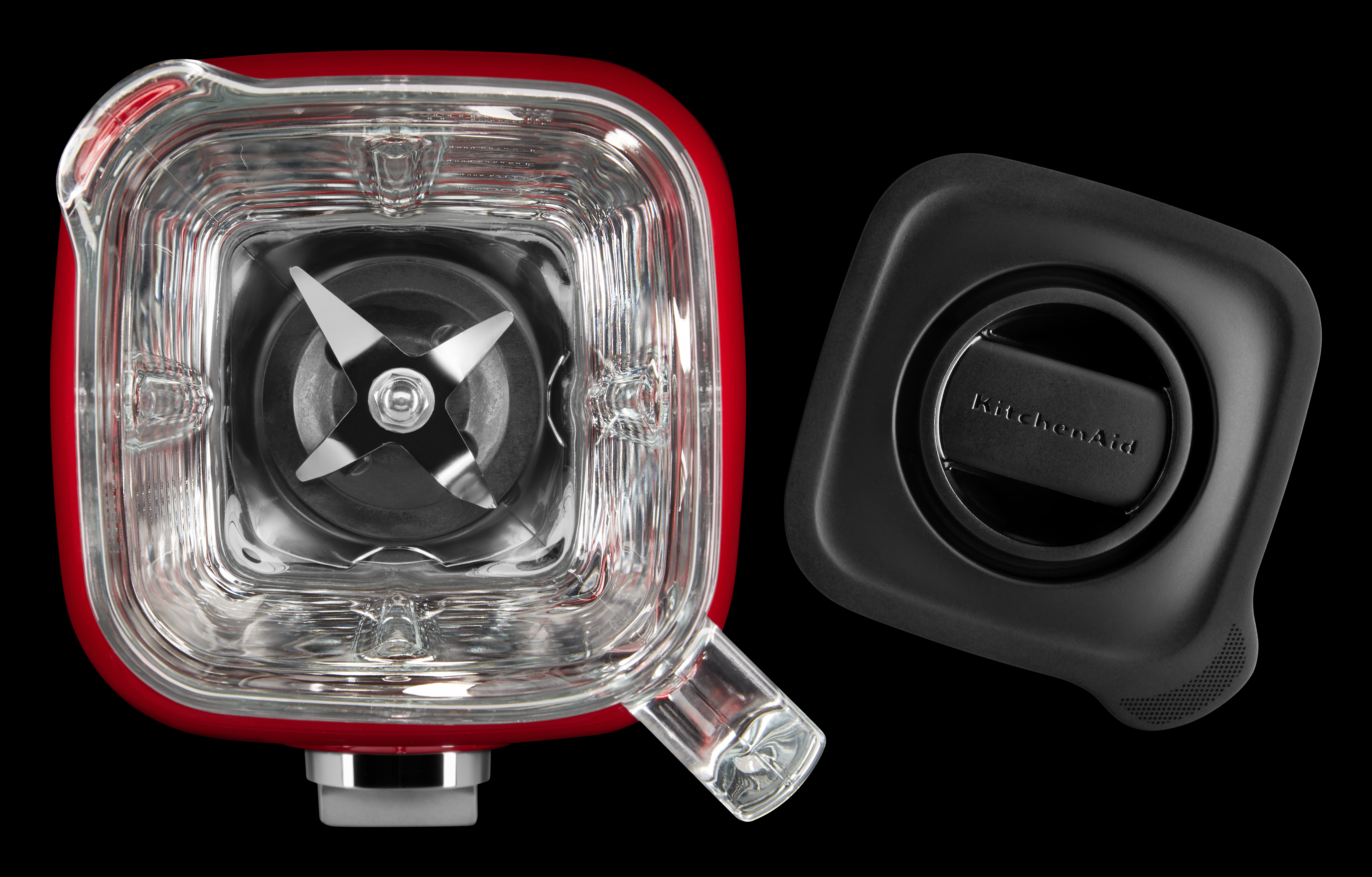 Roter KitchenAid-Mixer mit Klingen und schwarzem Deckel auf schwarzem Hintergrund.