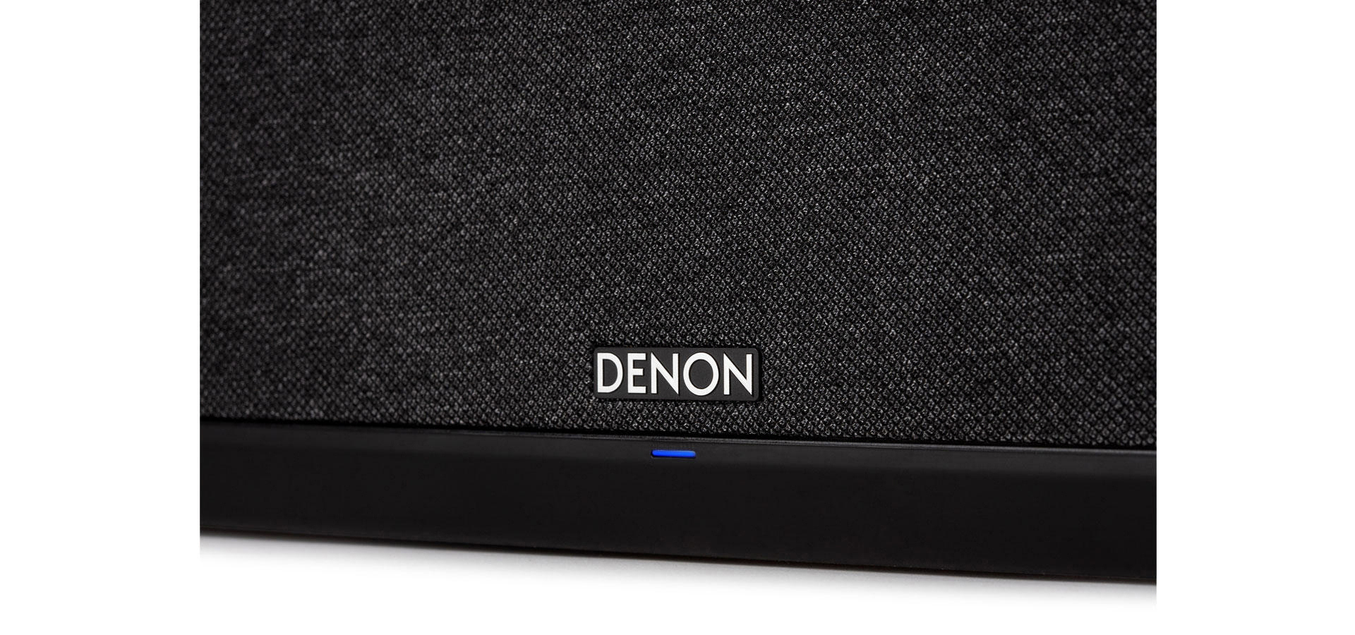 Nahaufnahme eines schwarzen Lautsprechers mit Denon-Logo und blauem Licht unten.