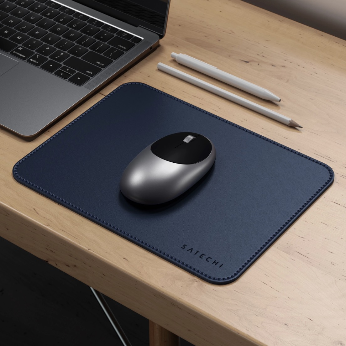 Une souris sans fil argentée, un tapis de souris bleu, un crayon et un stylo sur un bureau en bois.