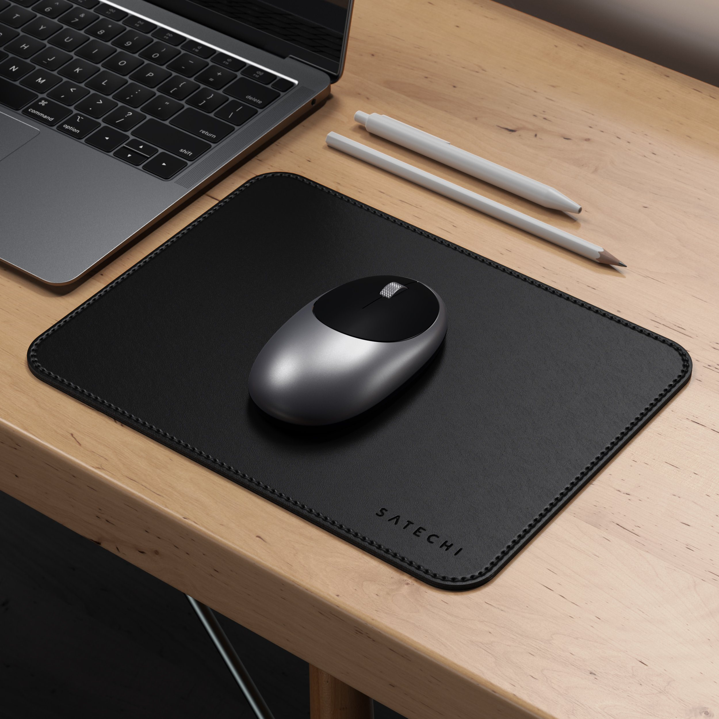 Mouse e tappetino neri con un laptop e una penna sullo sfondo.