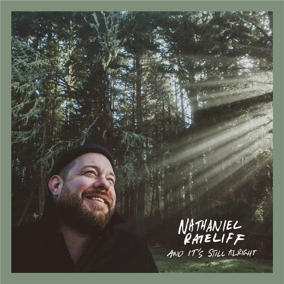 Homme souriant dans une forêt avec la lumière du soleil. Texte : 'Nathaniel Rateliff and It's Still Alright'.