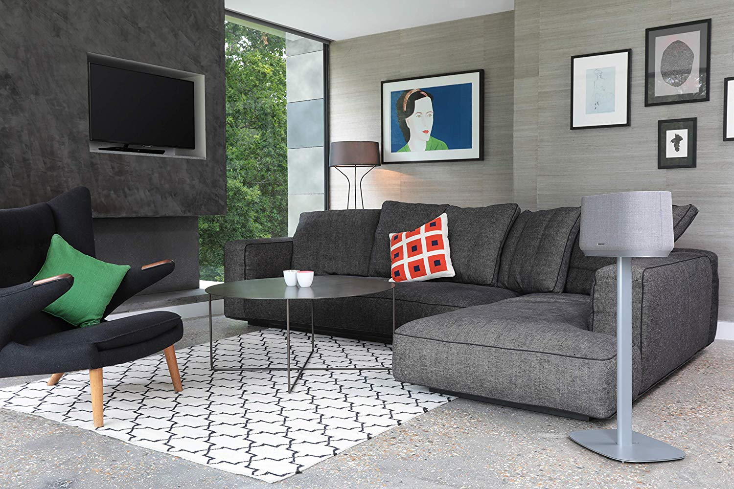 Een woonkamer met een donkergrijze bank, kunst en een moderne luidspreker.