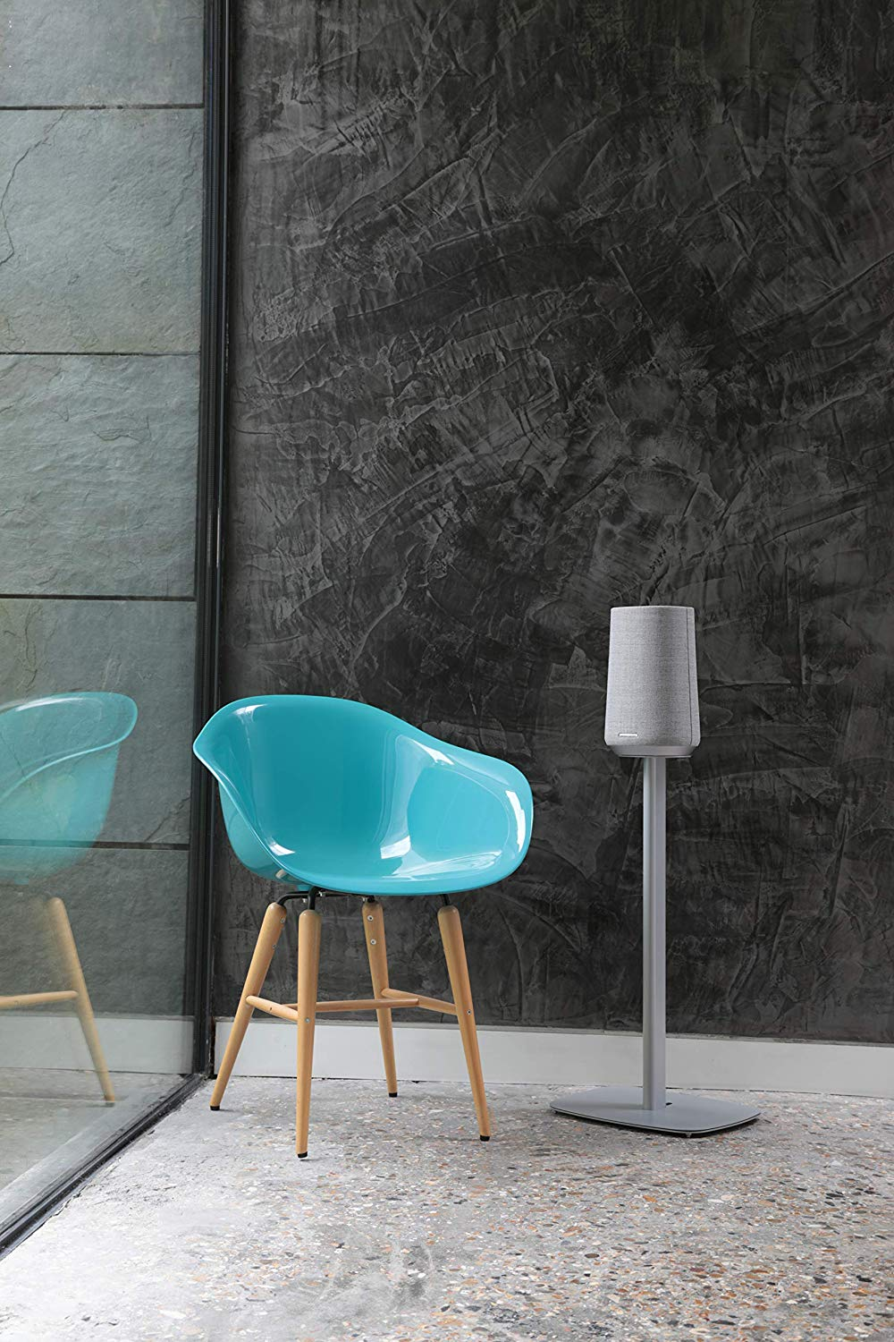 Een modern interieur met een blauwe stoel, een hoge speaker op een standaard en een glazen wand.