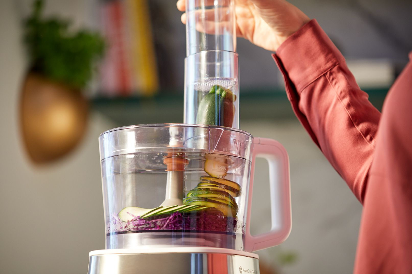 A hand is placing a zucchini into a food processor.