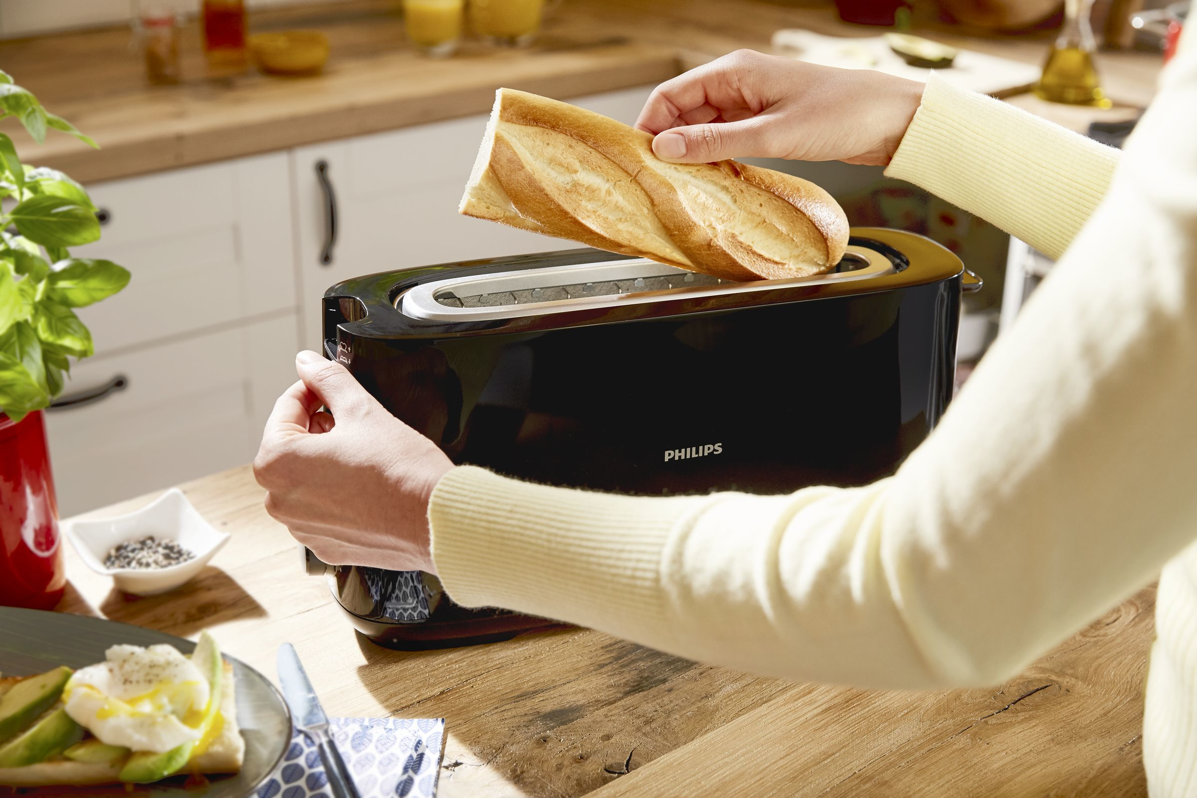A person is inserting bread into a black Philips toaster.