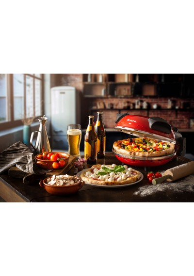 Egy képen egy asztal látható pizzával, sörrel, hozzávalókkal és egy piros pizzakészítővel.