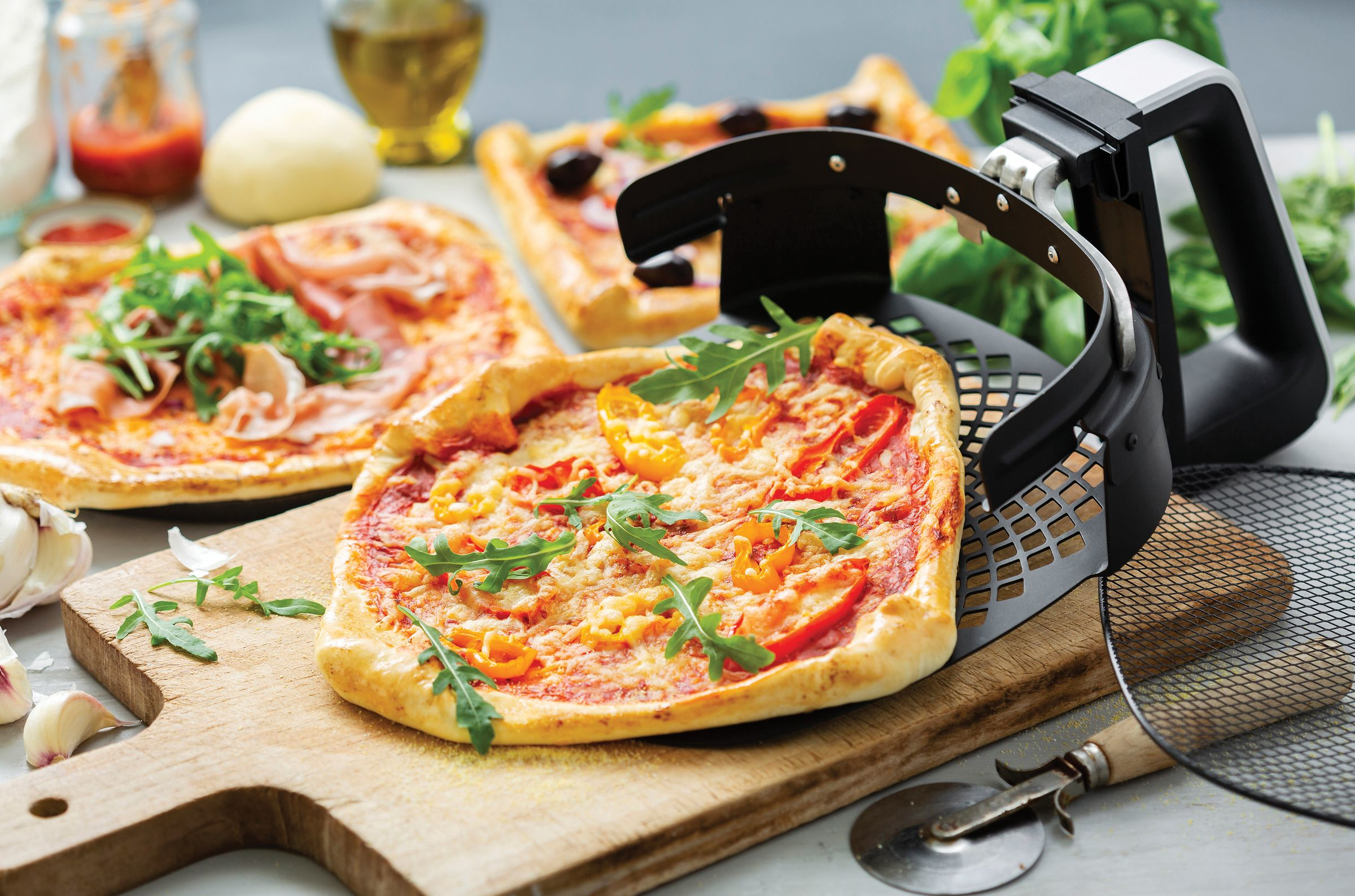 Pizza on a wooden board with fresh ingredients, near a pizza cutter and a container.