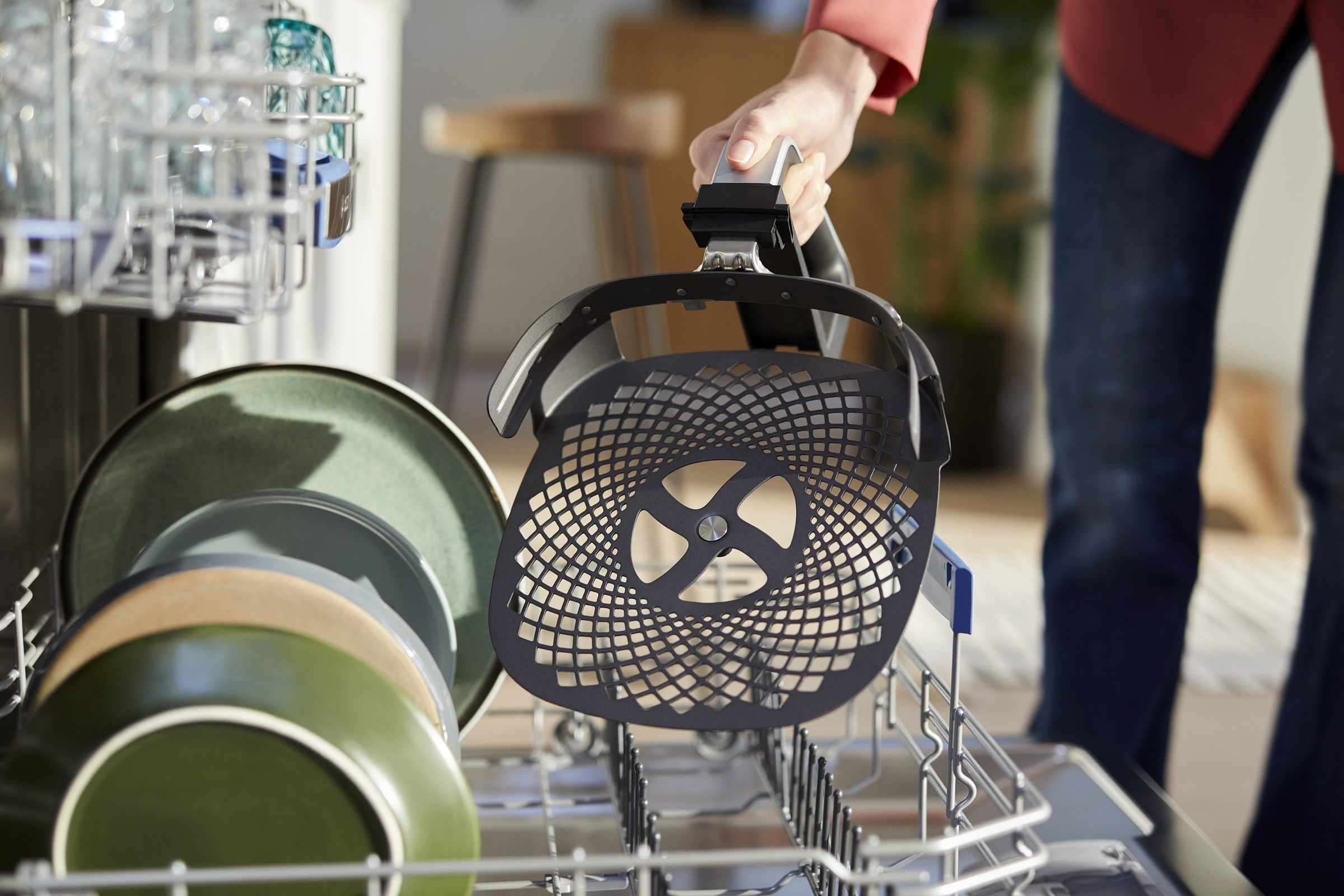 A person's hand holding a filter basket from a dishwasher.