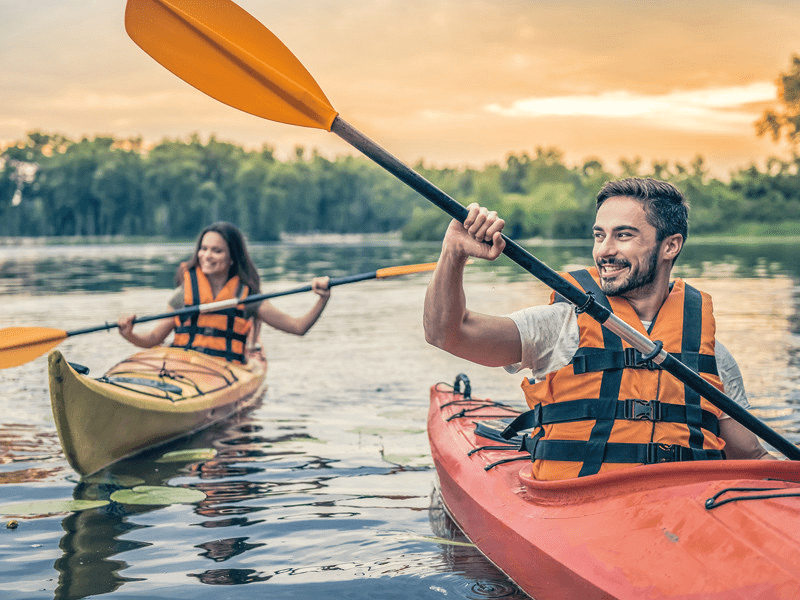 Un uomo e una donna in kayak con le pagaie. Tramonto sull'acqua sullo sfondo.
