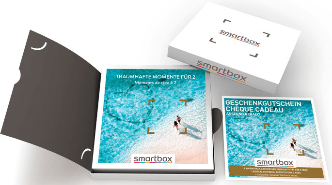 Un set regalo Smartbox con una scatola bianca, buoni regalo aperti e un'illustrazione di una spiaggia.