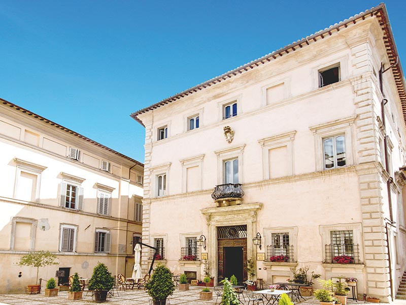 Un edificio color chiaro con un grande ingresso principale, circondato da un cortile quadrato.