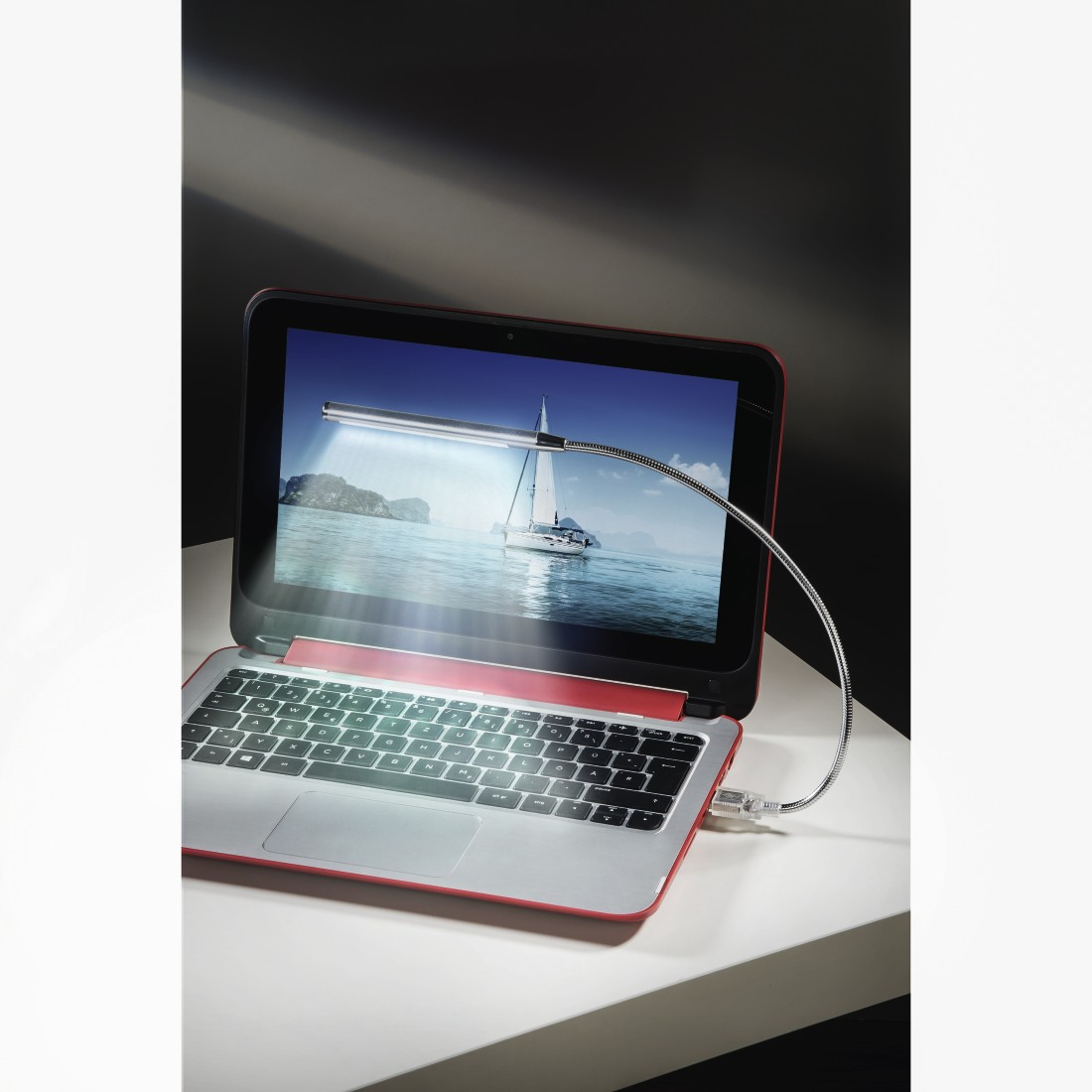 Laptop met een flexibele lamp bevestigd. Scherm toont een zeilboot.