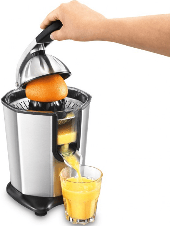 Una persona che sprema un'arancia in uno spremiagrumi, bicchiere di succo davanti.