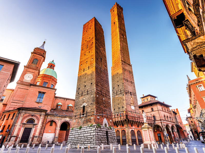 Due alte torri di mattoni in una città, con edifici e un cielo azzurro.