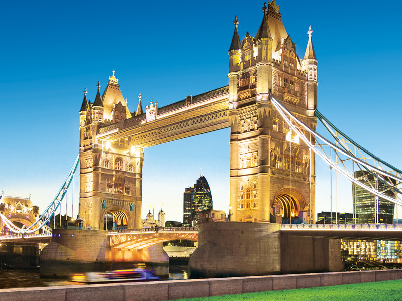 Tower Bridge a Londra al tramonto, con luci accese, cielo blu e una barca che passa.