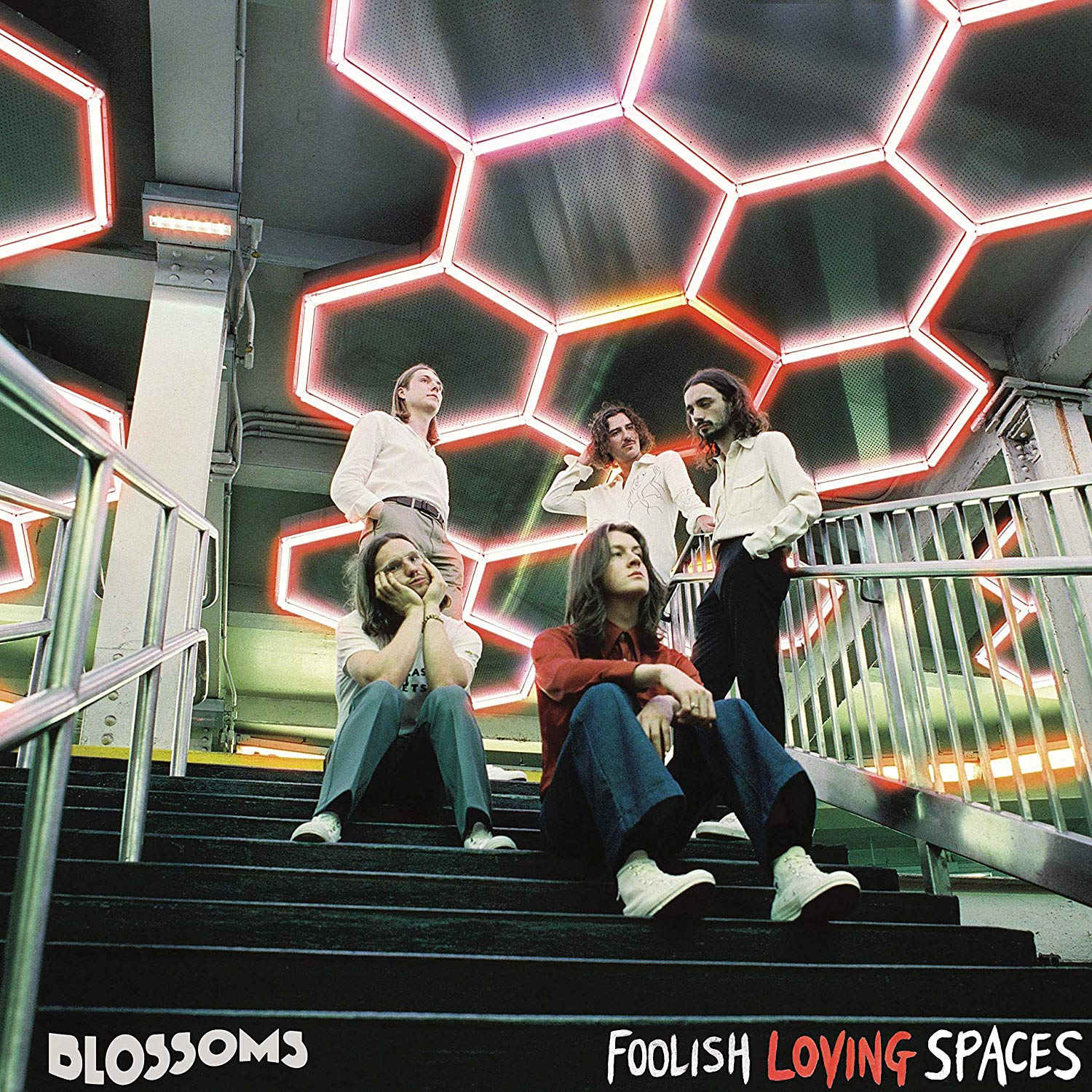 Album borító a zenekarral a lépcsőn neonfények alatt, melyek a 'Foolish Loving Spaces' feliratot mutatják.