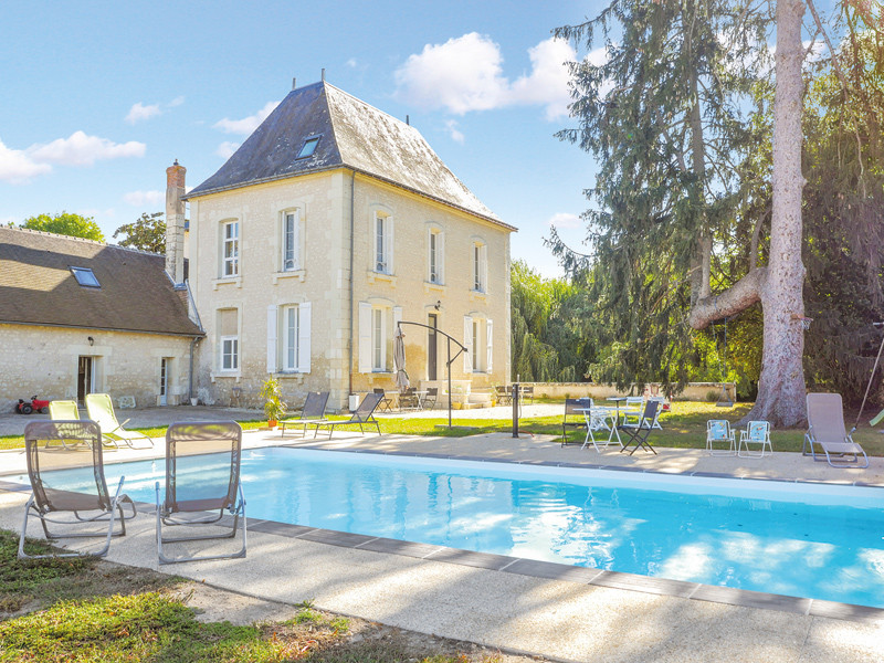 Scatto esterno di una grande casa con piscina, circondata da alberi e prato.