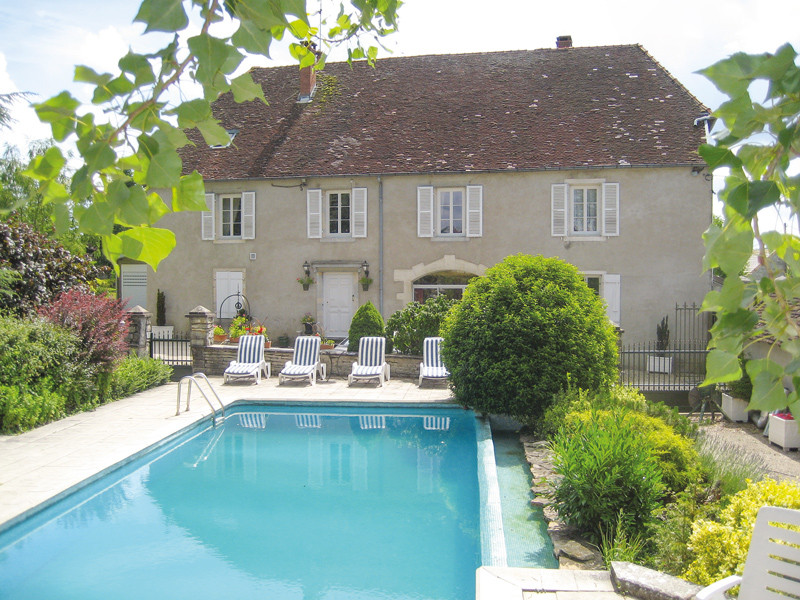 Casa con piscina, sedie e cespugli verdi, cielo blu.