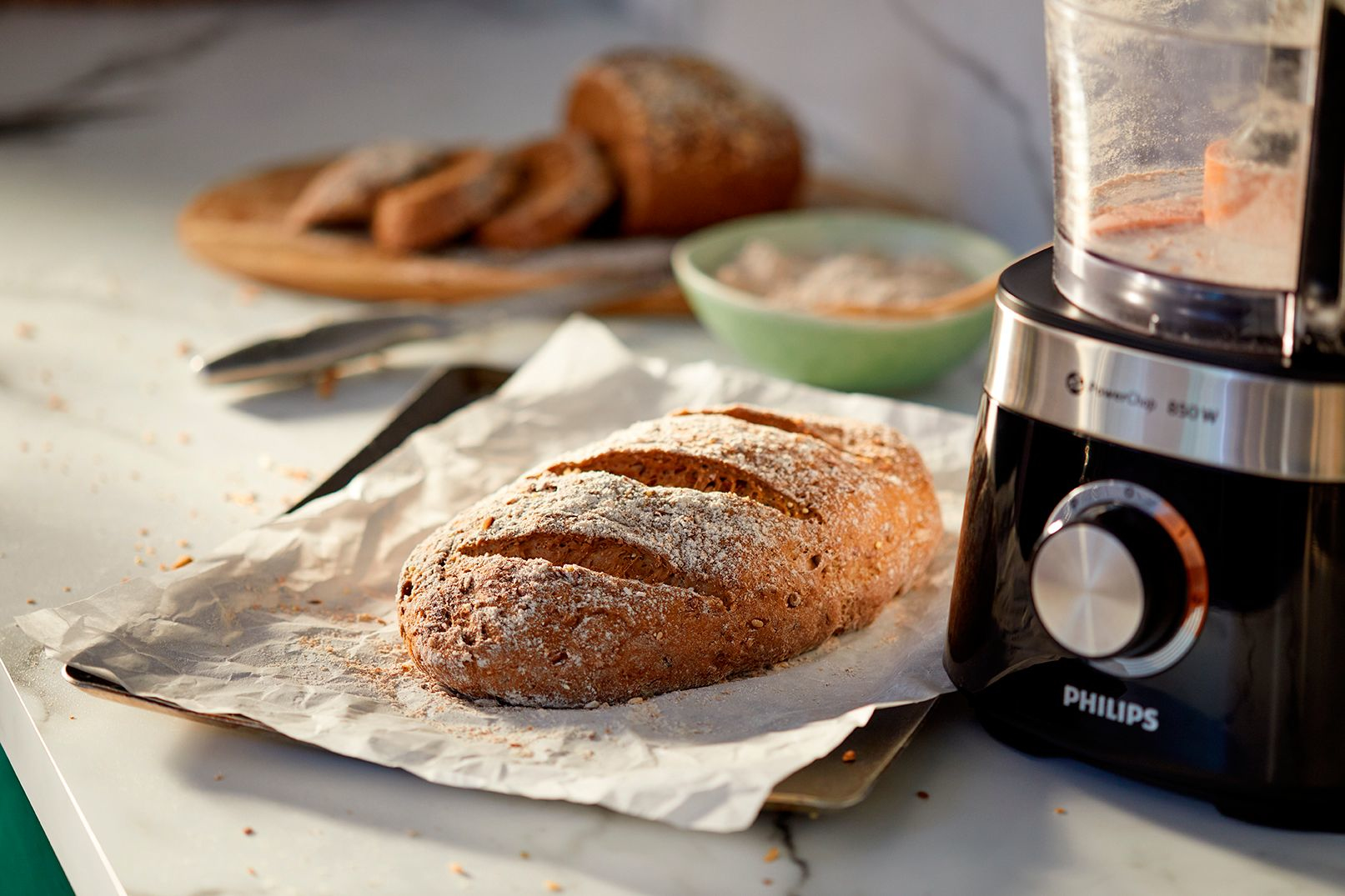 Brotlaib auf Pergamentpapier, mit Küchenmaschine und Brotscheiben.