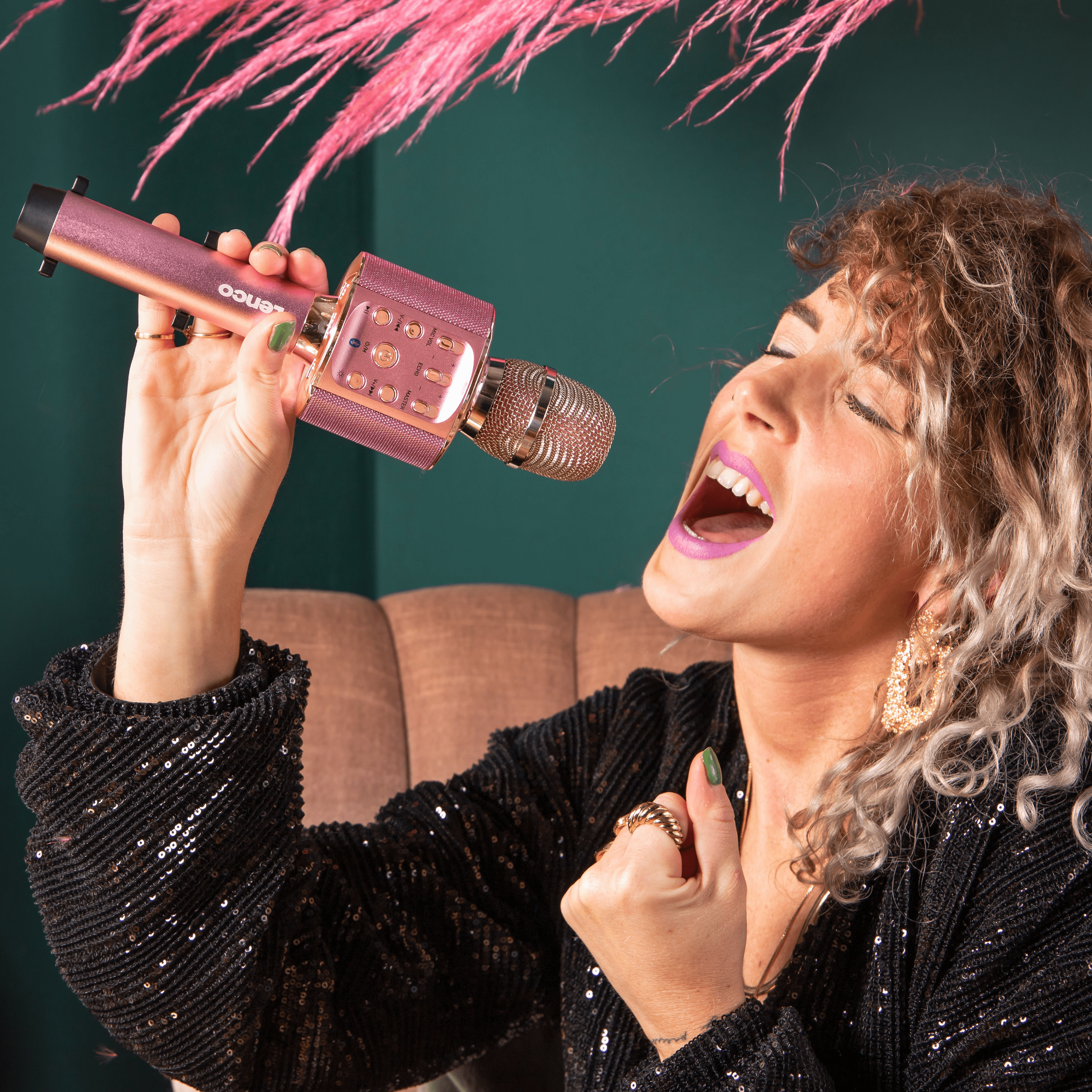 Femme chantant dans un microphone rose doré. Bouche ouverte, expression excitée.