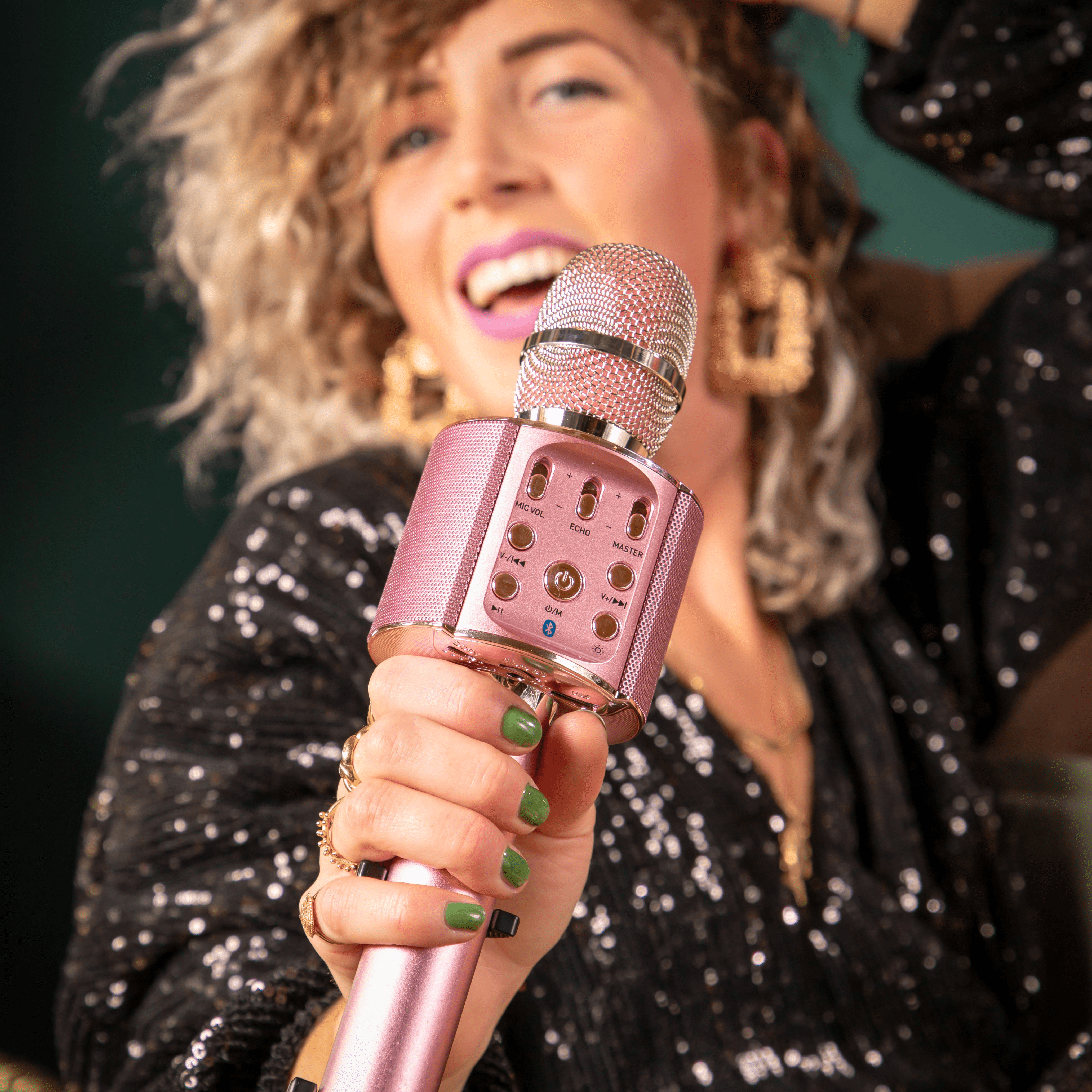 Une femme avec un microphone chante joyeusement, portant un haut noir à paillettes.