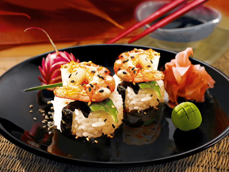 Sushi sur une assiette noire avec des baguettes rouges et une garniture au wasabi.