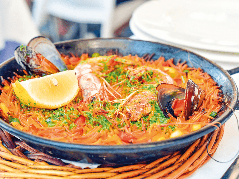 Paella dans une poêle noire, avec crevettes, moules, citron et persil.
