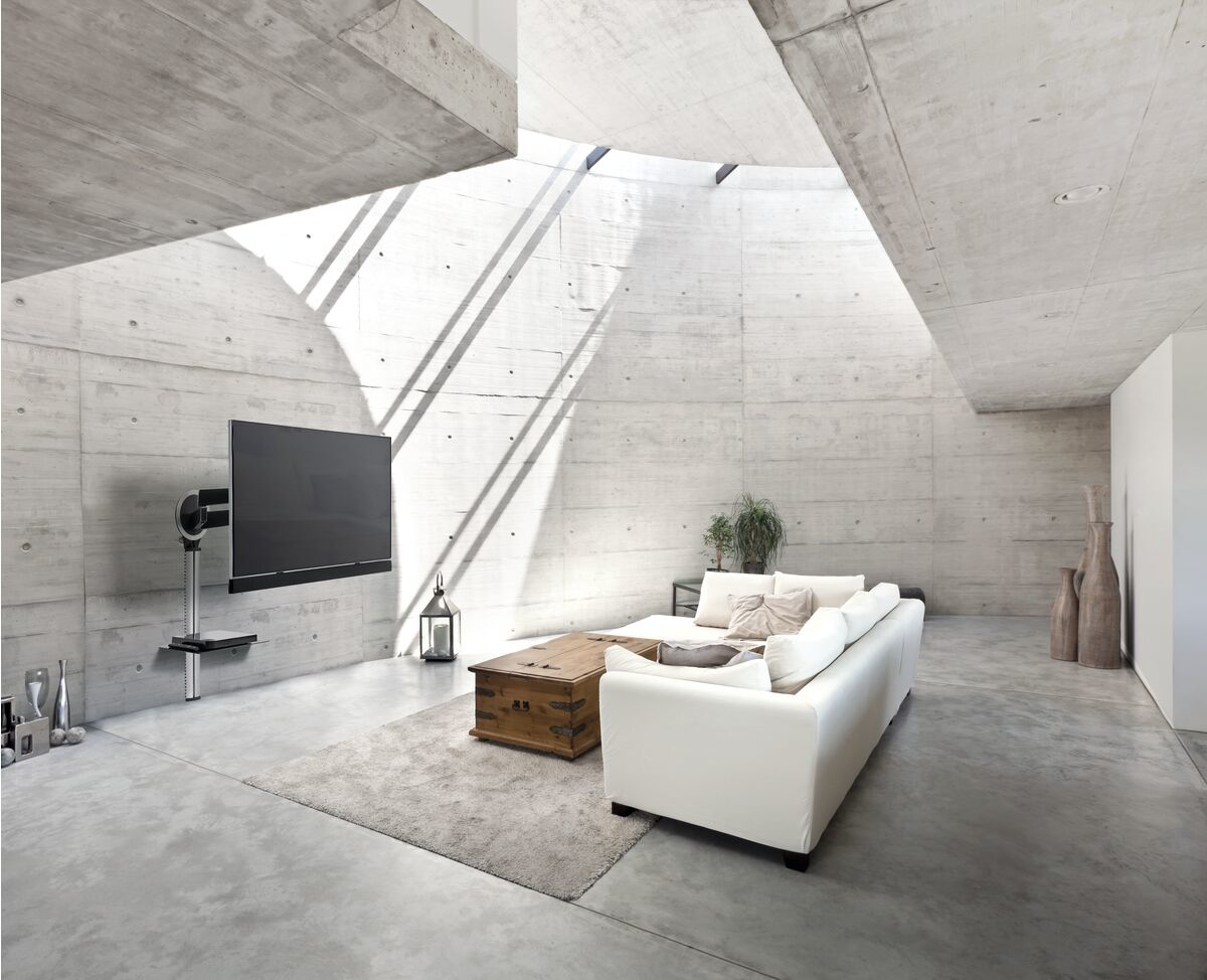 Salon moderne avec murs en béton, un canapé blanc et une grande télévision.