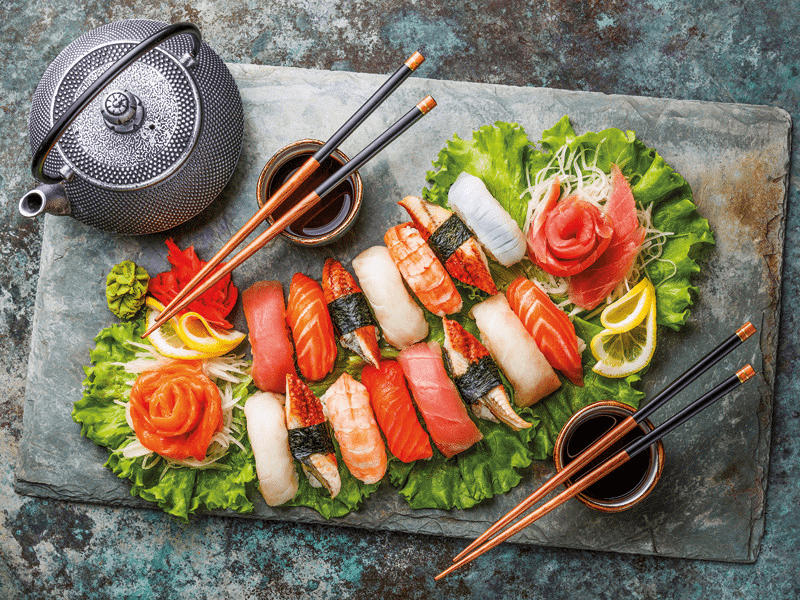 Sushi e cibo giapponese su un piatto di pietra. Bacchette, teiera e salsa.