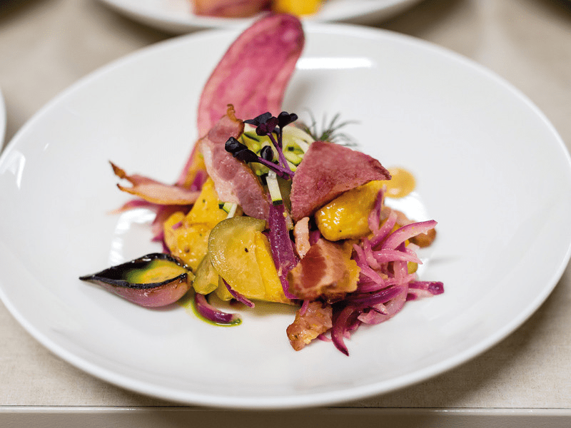 Piatto con cibo cotto: pancetta, cipolla viola e verdure gialle.