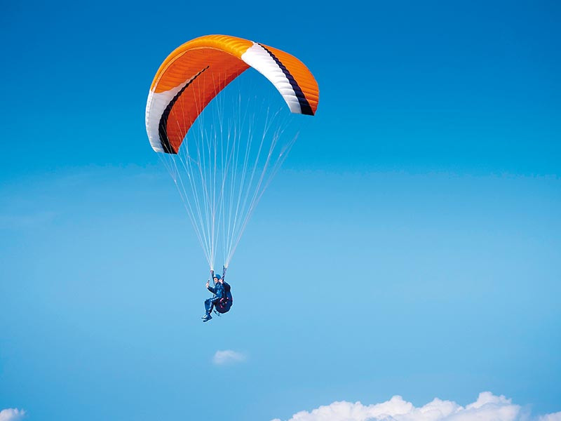 Un parapendio nel cielo con un'ala arancione e bianca contro un cielo blu.