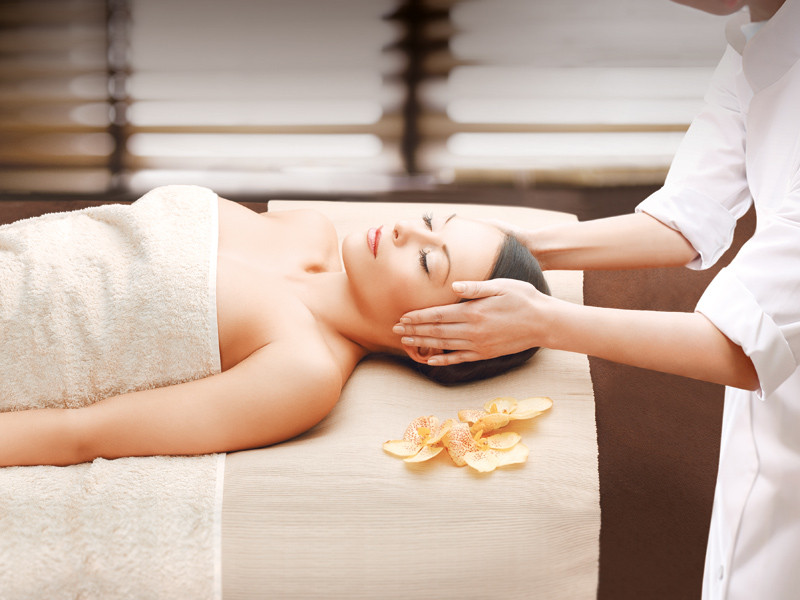 Donna che fa un trattamento spa. Una persona le massaggia la testa. Fiori sul lettino da massaggio.