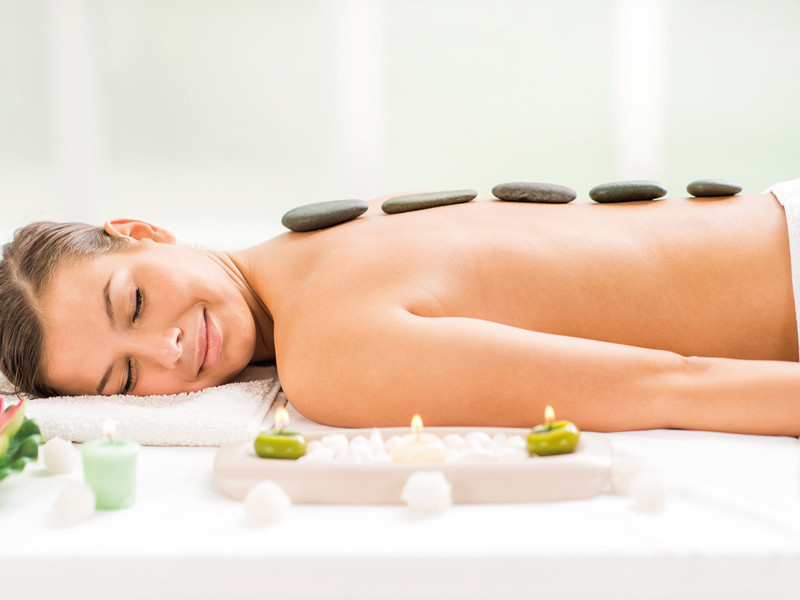 Femme allongée sur une table de massage avec des pierres sur le dos. Bougies devant.