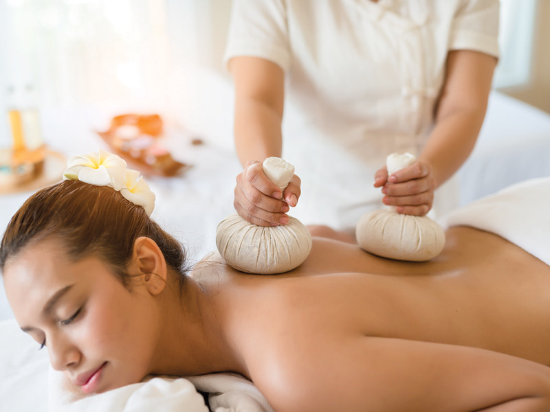 Une femme reçoit un massage du dos avec des boules de compression aux herbes chaudes.