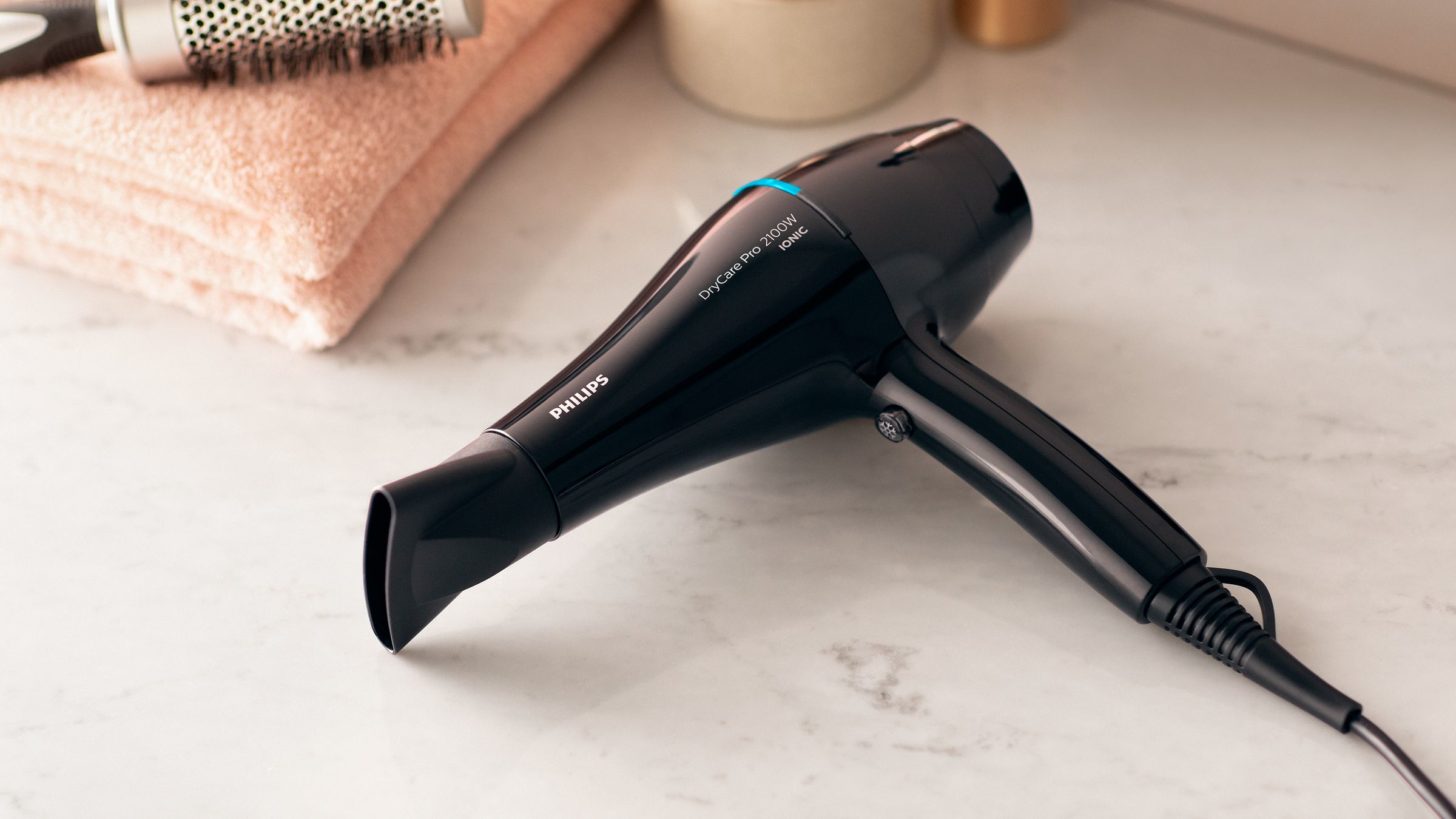 Black Philips hair dryer on a marble surface with a towel and brush.